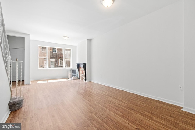 unfurnished living room featuring wood finished floors, baseboards, and a brick fireplace
