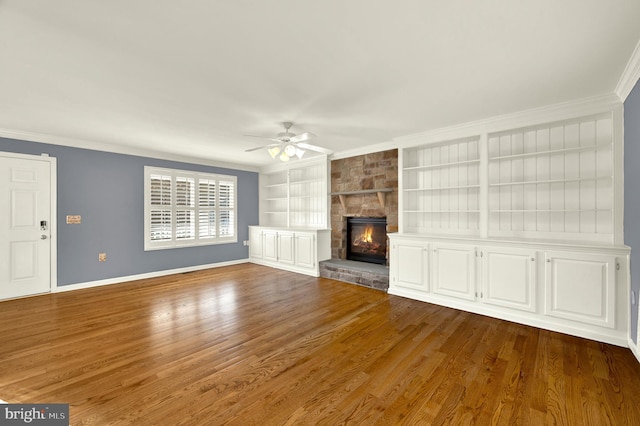 unfurnished living room featuring dark wood finished floors, baseboards, built in shelves, a ceiling fan, and crown molding