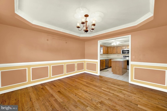 unfurnished dining area with a chandelier, a raised ceiling, light wood finished floors, and wainscoting