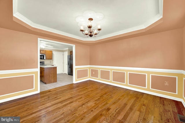 unfurnished dining area with a wainscoted wall, a tray ceiling, ornamental molding, light wood-style flooring, and a notable chandelier