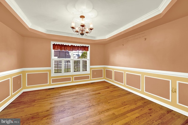 empty room with a raised ceiling, ornamental molding, and an inviting chandelier