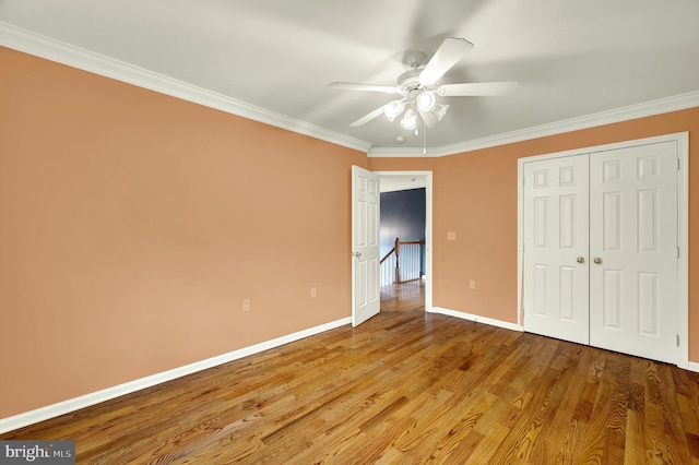 unfurnished bedroom with wood finished floors, a ceiling fan, a closet, crown molding, and baseboards