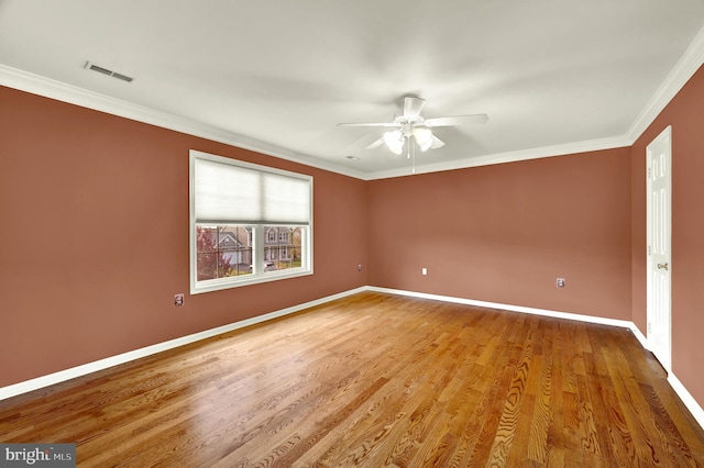 empty room featuring baseboards, visible vents, a ceiling fan, wood finished floors, and crown molding