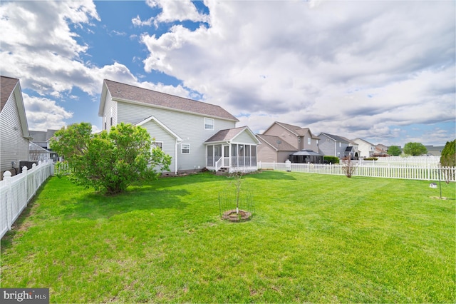 rear view of property with a fenced backyard, a sunroom, a yard, and a residential view