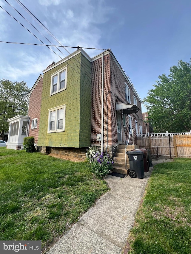 view of side of home with a lawn, fence, and brick siding