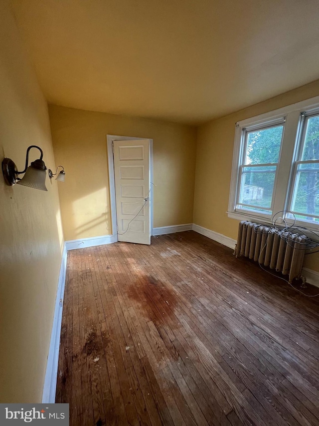 empty room featuring baseboards, radiator heating unit, and hardwood / wood-style flooring