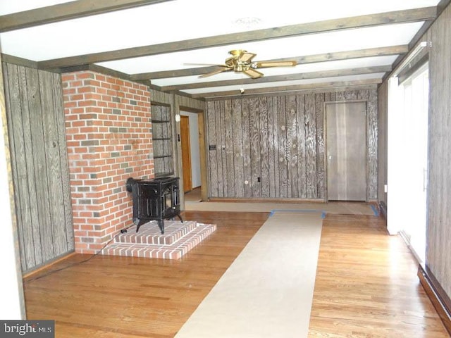 2560 Sardonyx Dr, Chambersburg, PA 17202 - unfurnished living room featuring ceiling fan, a wood stove, beamed ceiling, wood finished floors, and wooden walls