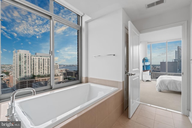 ensuite bathroom with tiled bath, a city view, and tile patterned flooring