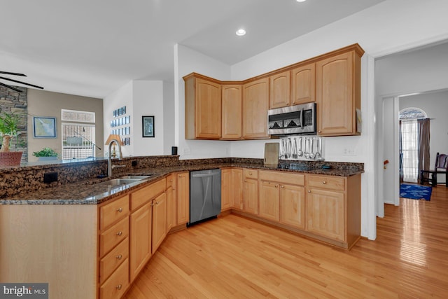 kitchen with dark stone counters, a sink, light wood-type flooring, a wealth of natural light, and stainless steel appliances