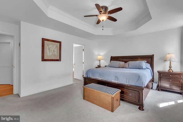 carpeted bedroom with ceiling fan, a tray ceiling, and ornamental molding