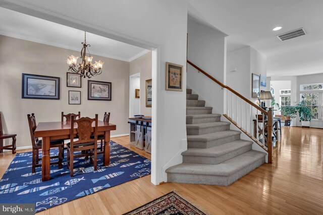dining area featuring stairway, wood finished floors, a chandelier, ornamental molding, and visible vents