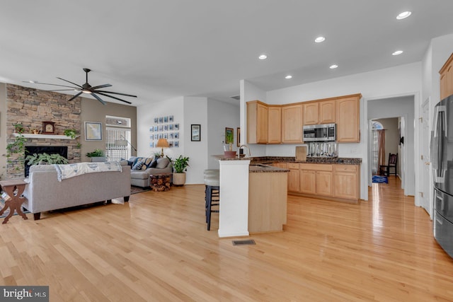 kitchen featuring light brown cabinets, stainless steel microwave, light wood-style flooring, open floor plan, and ceiling fan