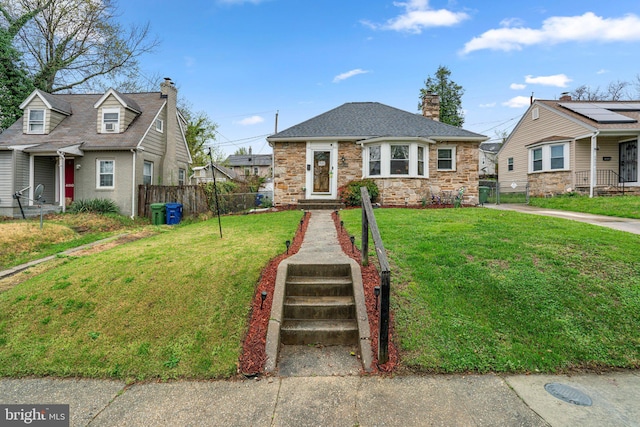 bungalow-style house with fence, a front yard, stone siding, and a chimney