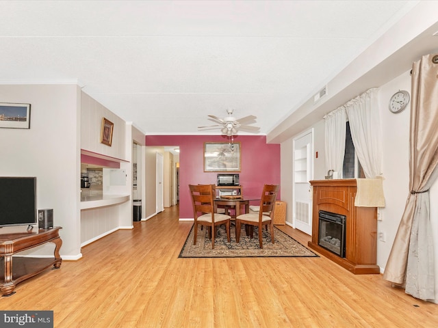 dining room with a glass covered fireplace, baseboards, light wood-type flooring, built in features, and ceiling fan
