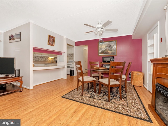 dining area with a fireplace, ornamental molding, a ceiling fan, wood finished floors, and baseboards