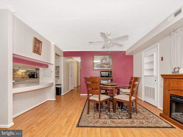 dining area featuring baseboards, a fireplace, light wood-style floors, visible vents, and ceiling fan