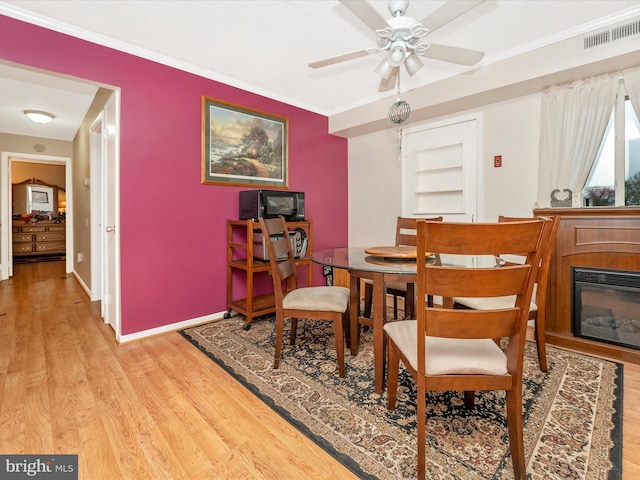 dining room featuring visible vents, a ceiling fan, crown molding, wood finished floors, and a glass covered fireplace