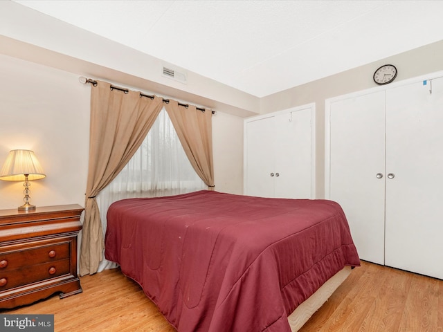 bedroom with visible vents, light wood-type flooring, and two closets