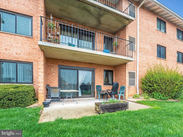rear view of property with brick siding, a lawn, a balcony, and a patio area
