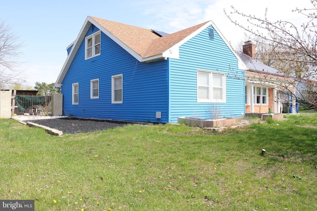 back of house with a lawn, a shingled roof, and a chimney