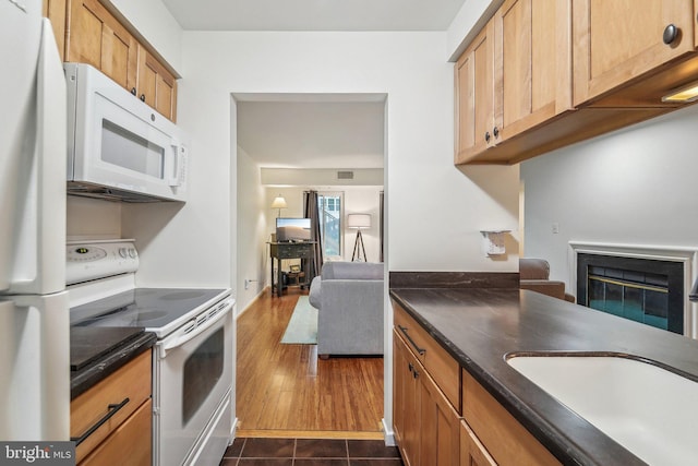 kitchen featuring brown cabinetry, dark wood-style flooring, dark countertops, a glass covered fireplace, and white appliances