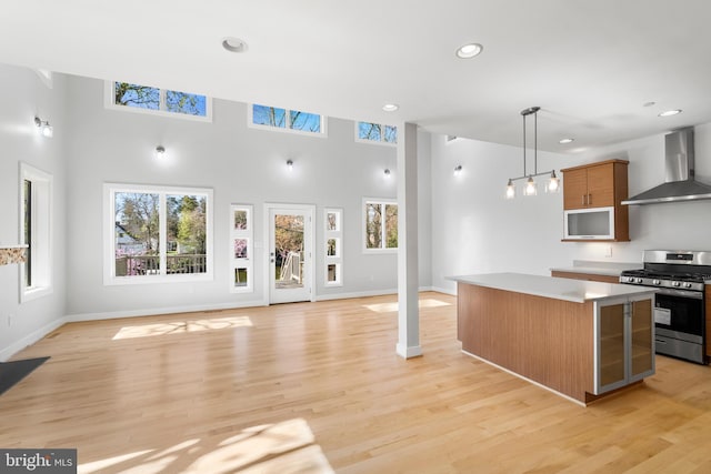 kitchen with stainless steel range with gas stovetop, a center island, wall chimney range hood, light countertops, and a healthy amount of sunlight