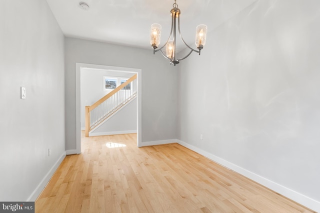 empty room with stairs, a notable chandelier, baseboards, and wood finished floors