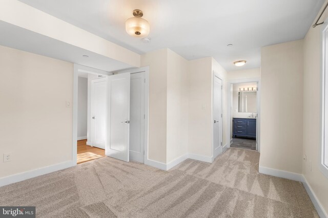 unfurnished bedroom with light carpet, ensuite bathroom, and baseboards