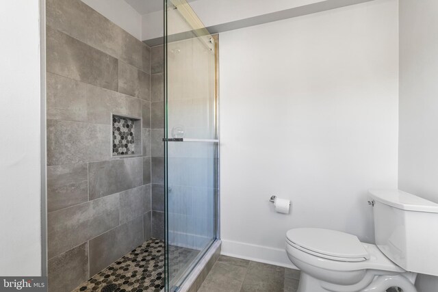 full bathroom featuring a tile shower, toilet, tile patterned flooring, and baseboards