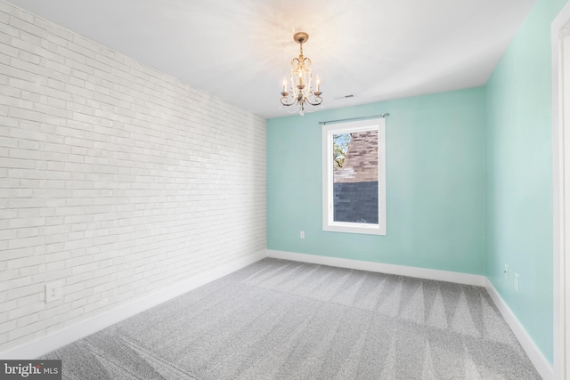 spare room with brick wall, a notable chandelier, baseboards, and carpet floors