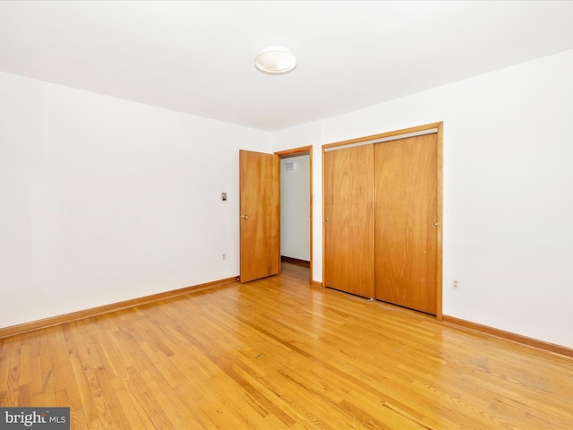 unfurnished bedroom featuring light wood-style floors, baseboards, and a closet