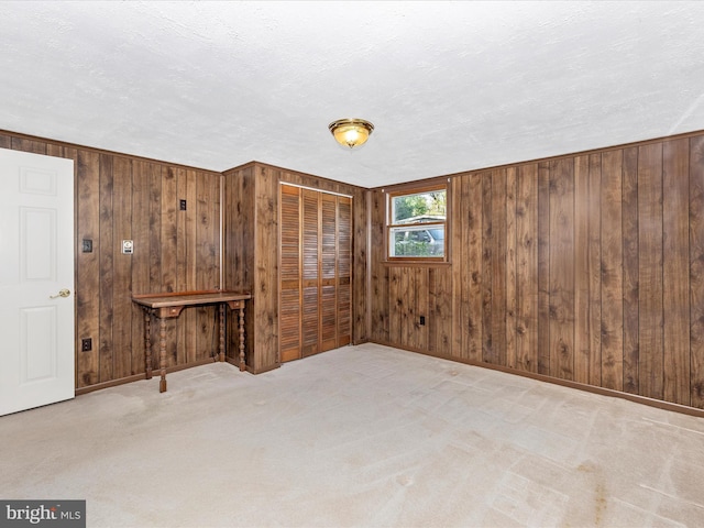 carpeted spare room featuring wooden walls, a textured ceiling, and baseboards