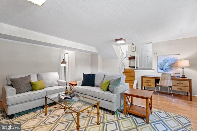 living room featuring a textured ceiling, stairway, and light wood-type flooring