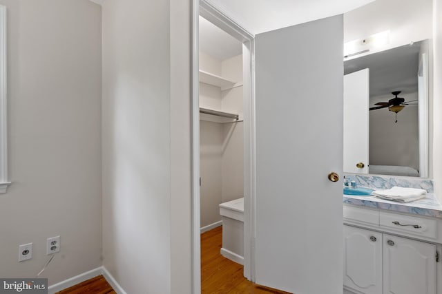 bathroom featuring ceiling fan, vanity, baseboards, wood finished floors, and ensuite bathroom