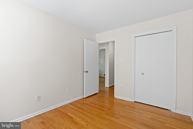 unfurnished bedroom with a closet, baseboards, and light wood-type flooring