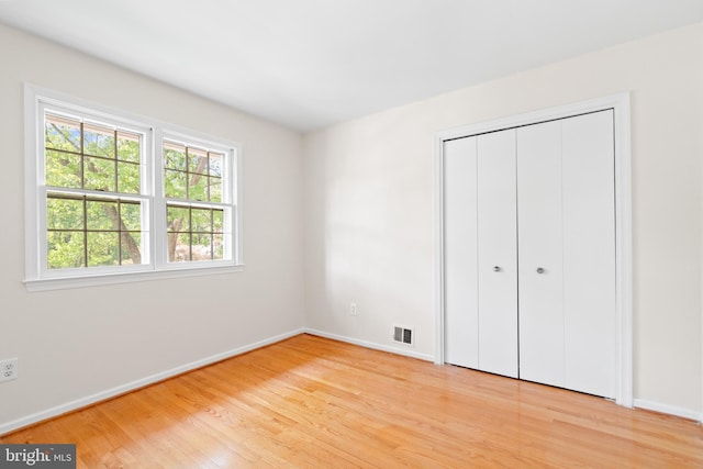 unfurnished bedroom with baseboards, visible vents, wood finished floors, and a closet