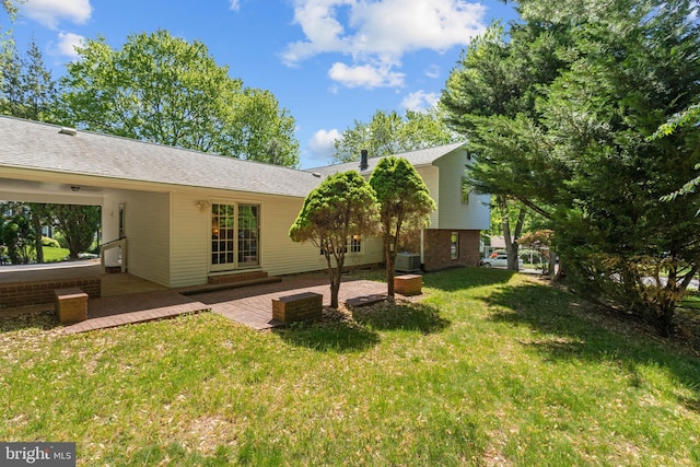 rear view of property featuring a yard, a patio, and roof with shingles