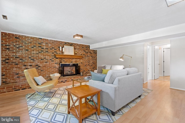 living room featuring light wood-style floors, a textured ceiling, a brick fireplace, and brick wall