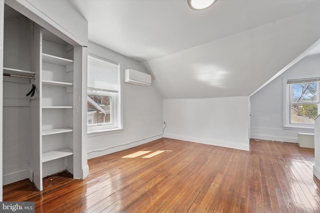additional living space with a wall mounted air conditioner, wood-type flooring, baseboards, and vaulted ceiling