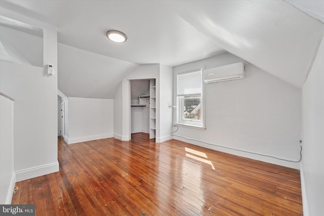 additional living space featuring a wall mounted air conditioner, baseboards, hardwood / wood-style flooring, and vaulted ceiling