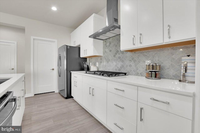 kitchen featuring wall chimney range hood, appliances with stainless steel finishes, decorative backsplash, and white cabinetry