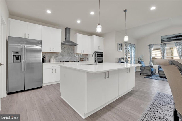 kitchen featuring wall chimney range hood, a sink, light wood-style flooring, backsplash, and stainless steel refrigerator with ice dispenser