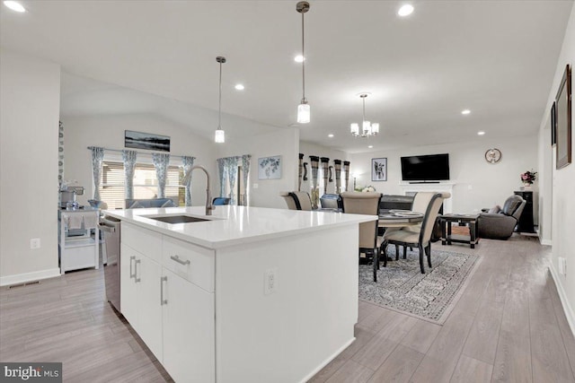 kitchen featuring stainless steel dishwasher, light wood-style floors, open floor plan, a center island with sink, and a sink