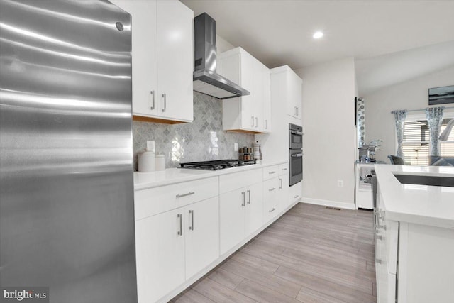 kitchen featuring wall chimney range hood, decorative backsplash, gas stovetop, a sink, and freestanding refrigerator