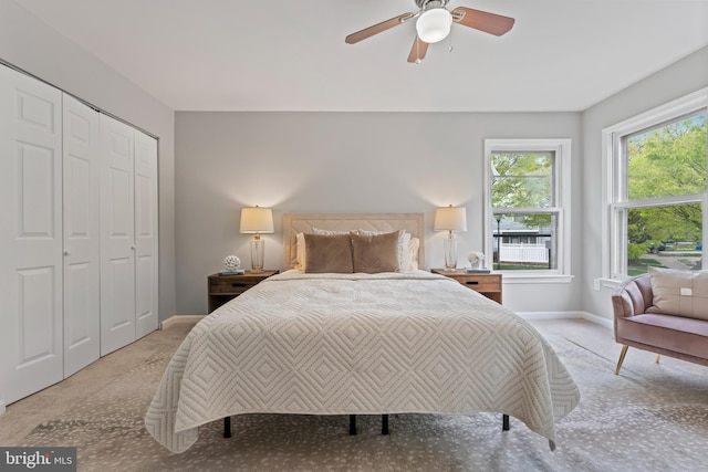 bedroom with a closet, light colored carpet, baseboards, and ceiling fan