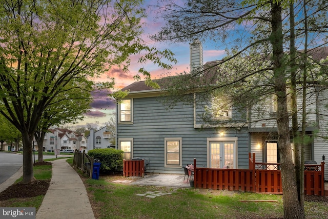back of property at dusk with french doors, a wooden deck, and a chimney