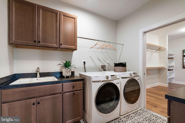 laundry area with baseboards, independent washer and dryer, cabinet space, light wood finished floors, and a sink