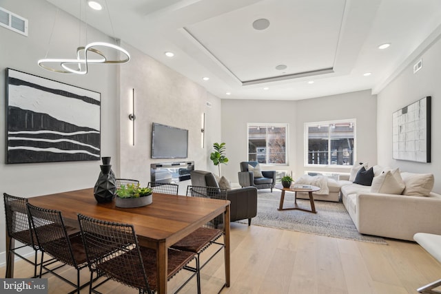 living area featuring a raised ceiling, light wood finished floors, visible vents, and recessed lighting