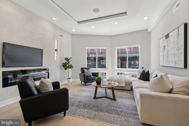 living room featuring a tray ceiling, wood finished floors, baseboards, and visible vents