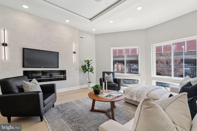 living area featuring visible vents, baseboards, light wood-style floors, a tray ceiling, and recessed lighting